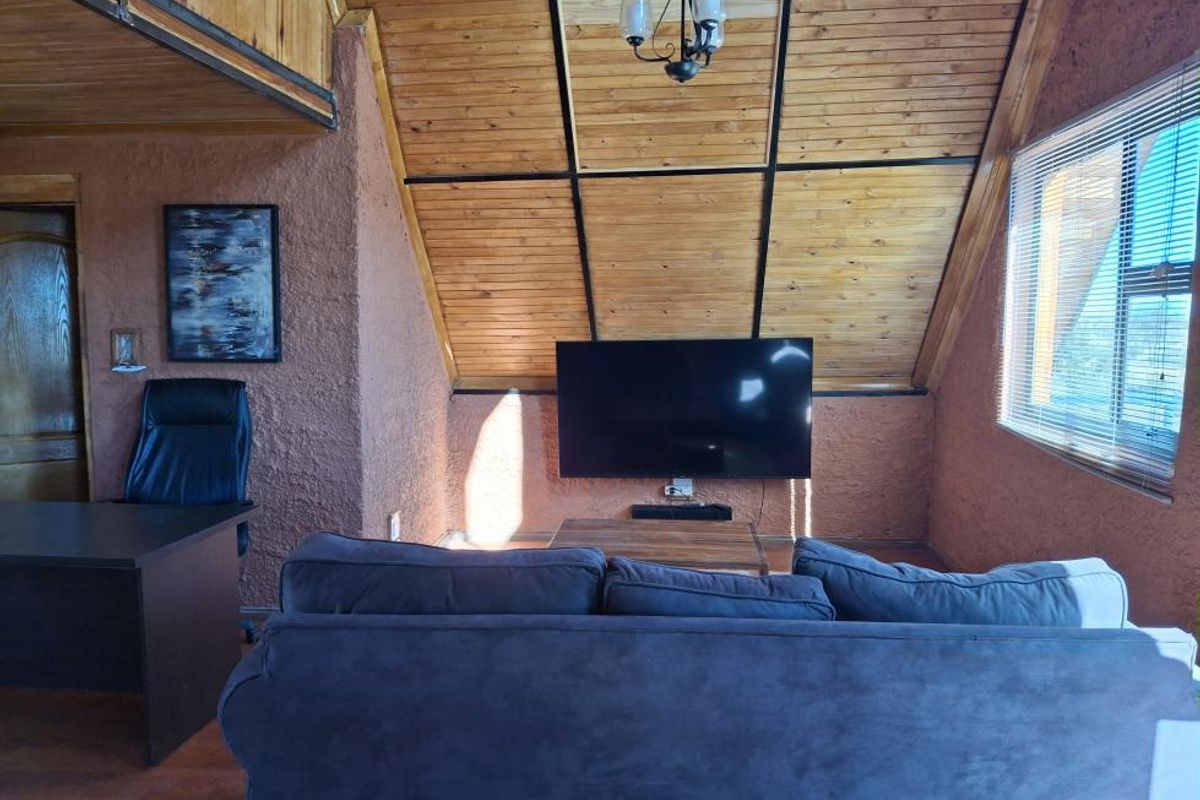 A cozy living area featuring a vaulted timber-clad ceiling, textured walls, and large windows, creating a warm and rustic atmosphere.