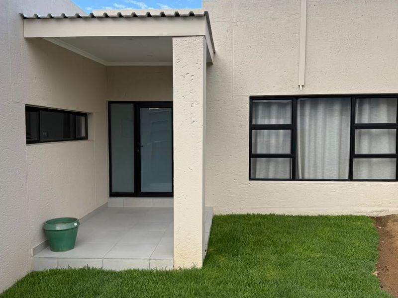 A clean rear exterior view featuring a covered patio area, modern aluminium window frames, and a well-maintained lawn.