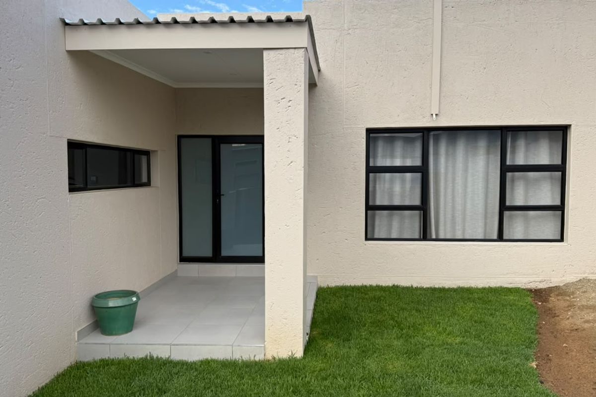 A clean rear exterior view featuring a covered patio area, modern aluminium window frames, and a well-maintained lawn.