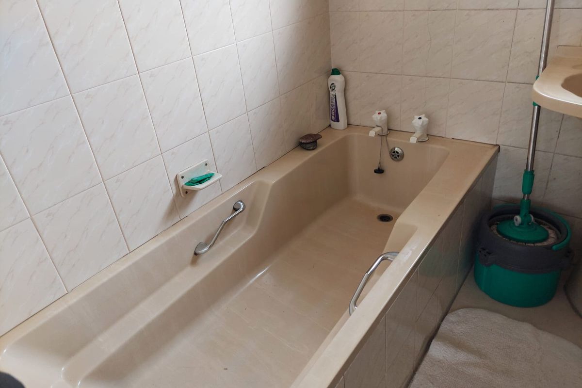 A dated bathroom featuring a built-in bathtub with chrome grab rails and tiled wall surrounds.