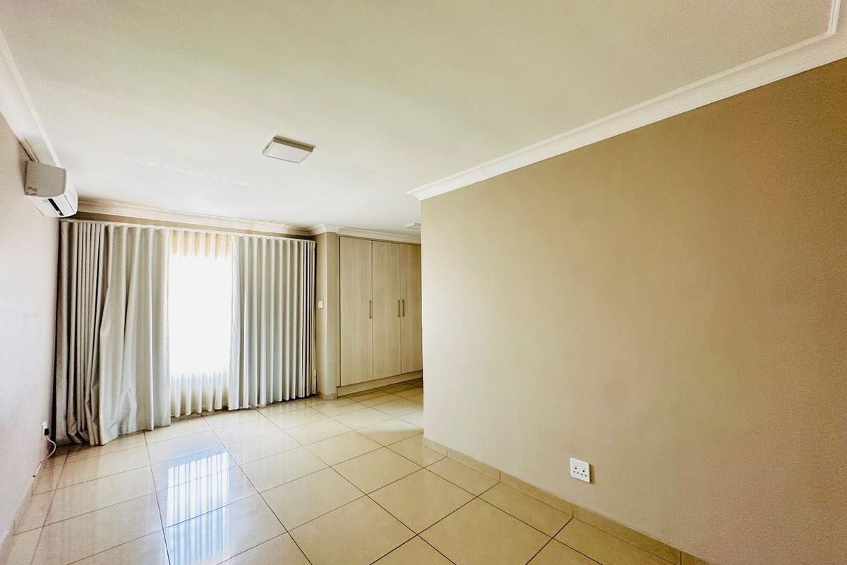 A bright, empty bedroom featuring neutral tiled flooring, built-in wooden cabinetry, and a wall-mounted air conditioning unit.