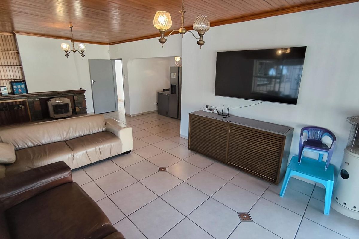Spacious living room featuring a timber ceiling, tiled flooring, and a stone fireplace, offering a functional layout with direct access to adjacent areas.