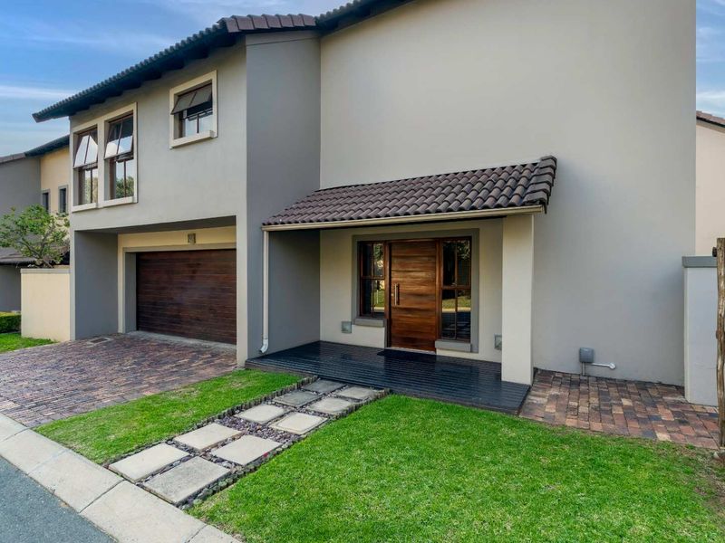 Modern double-storey home exterior featuring a paved driveway, integrated double garage, timber entrance deck, and a well-maintained front garden with stone pathway.