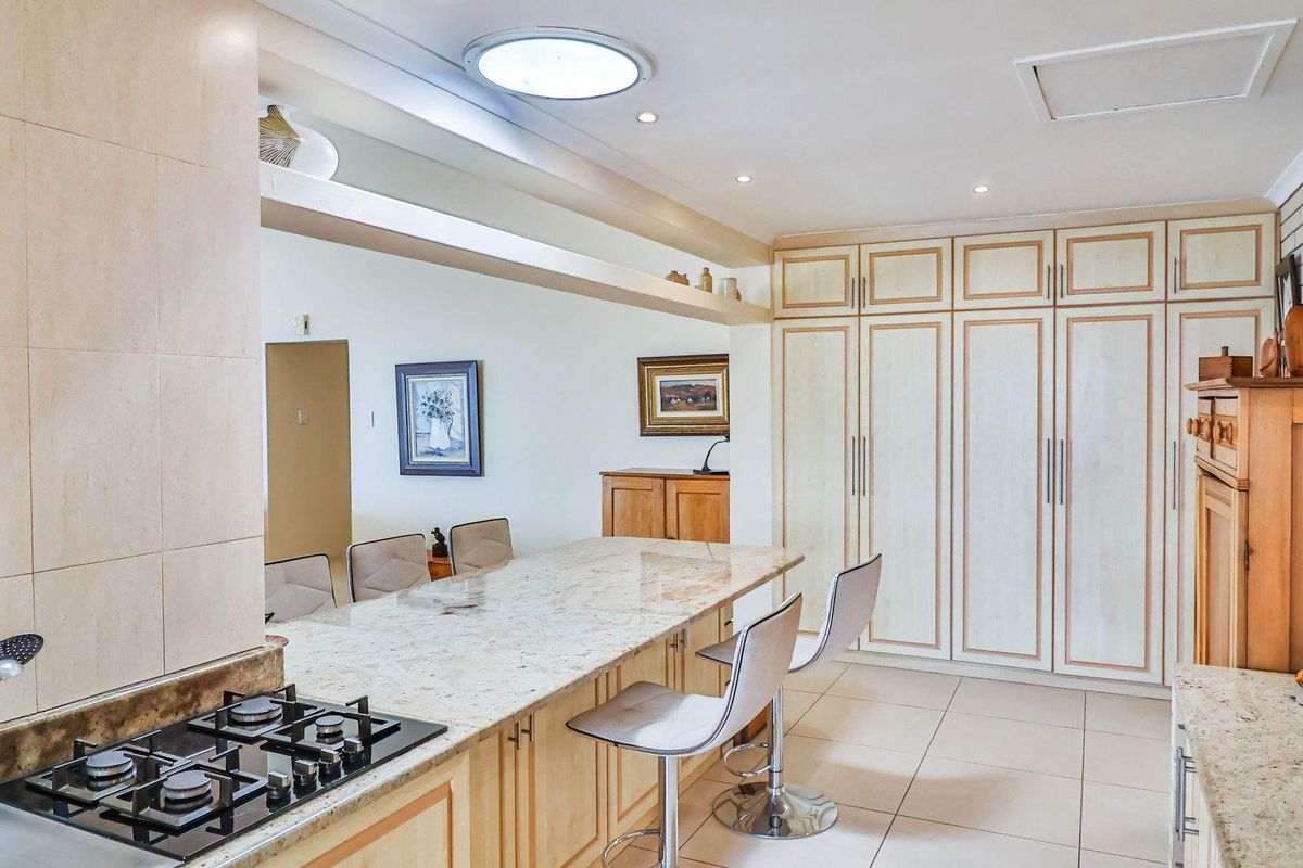 A spacious kitchen featuring light wood cabinetry, granite countertops, a built-in gas hob, and ample storage space with integrated cupboards.