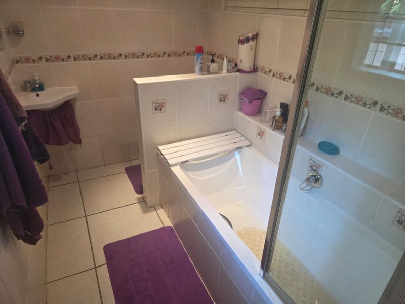 A functional bathroom featuring a built-in bathtub, corner basin, and tiled finishes throughout, offering a classic layout ready for modern updates.
