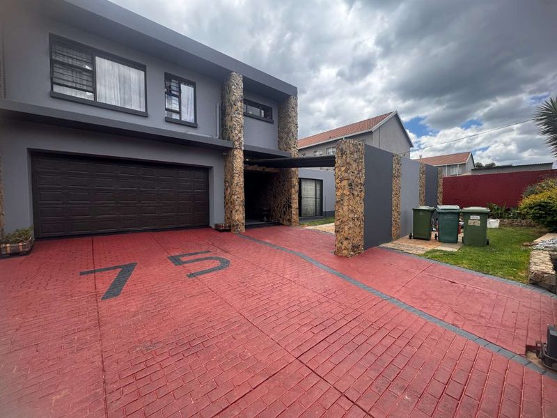 Modern double-storey home exterior featuring stone-clad pillars, a spacious paved driveway, and a secure double garage.