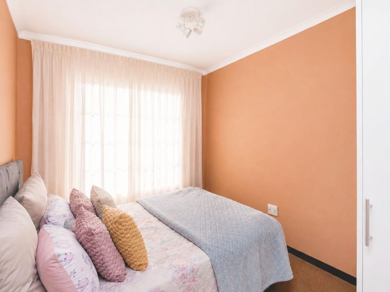 A cozy bedroom featuring carpeted flooring, a built-in wardrobe, and natural light filtered through window curtains.