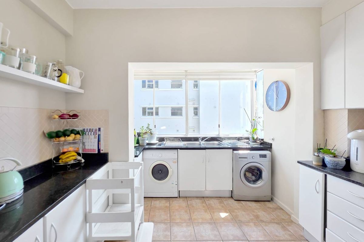 A bright, functional kitchen featuring white cabinetry, black granite countertops, a stainless steel sink, and tiled flooring with a large window for natural light.