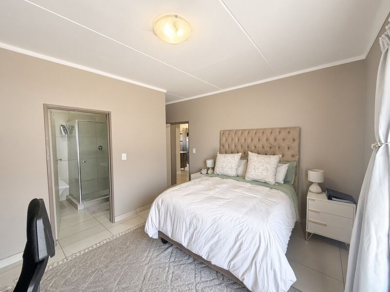 A well-maintained bedroom featuring neutral wall tones, tiled flooring, and an attached en-suite bathroom with a glass-enclosed shower.