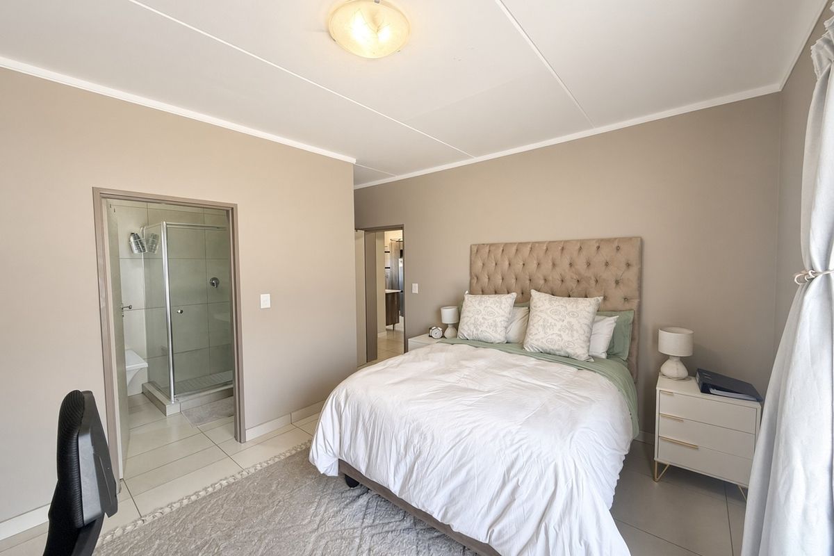 A well-maintained bedroom featuring neutral wall tones, tiled flooring, and an attached en-suite bathroom with a glass-enclosed shower.