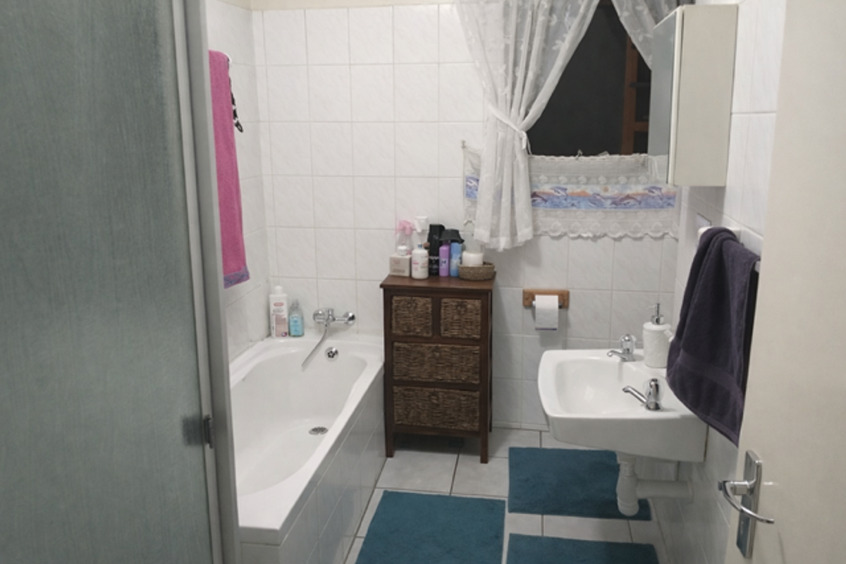 A functional bathroom featuring a built-in bathtub, wall-mounted basin, and tiled walls.