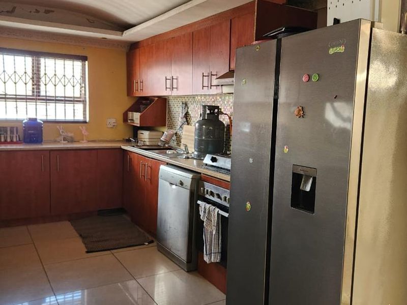A functional kitchen featuring wood-tone cabinetry, tiled flooring, and security bars on the window, offering a practical layout for daily meal preparation.