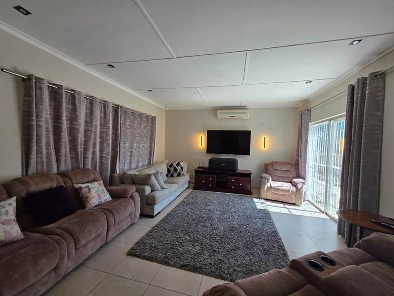 A comfortable living room featuring tiled flooring, recessed lighting, a wall-mounted air conditioner, and sliding glass doors leading to the exterior.