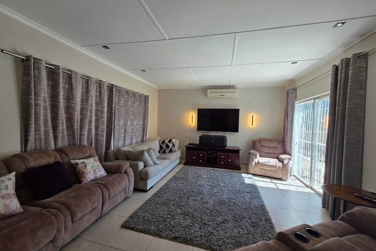 A comfortable living room featuring tiled flooring, recessed lighting, a wall-mounted air conditioner, and sliding glass doors leading to the exterior.