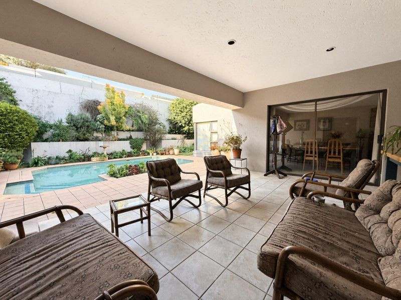 Covered outdoor patio featuring tiled flooring and recessed lighting, overlooking a private swimming pool and landscaped garden area.