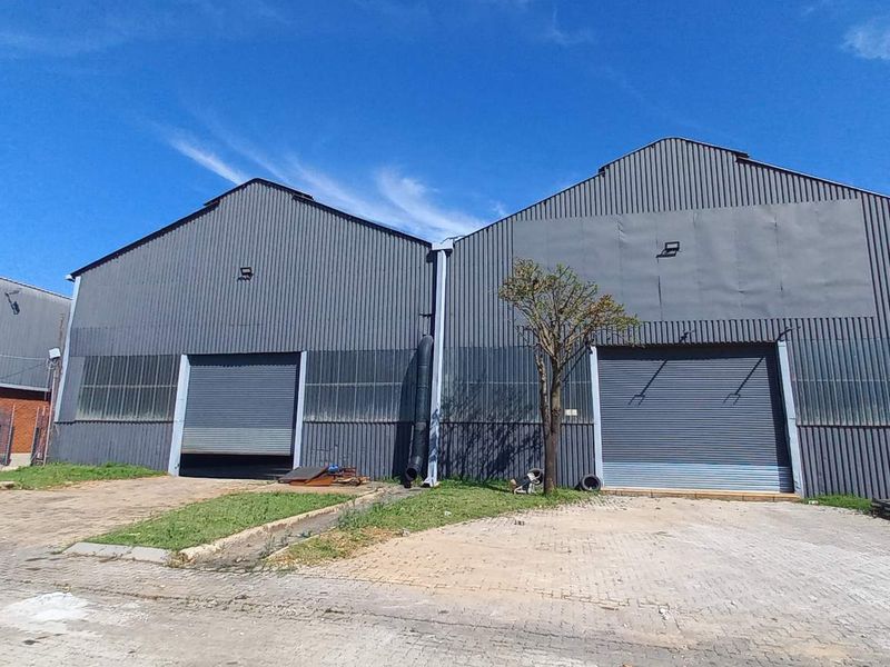 Industrial warehouse facility featuring dual roller shutter doors, corrugated metal exterior cladding, and a paved forecourt area.