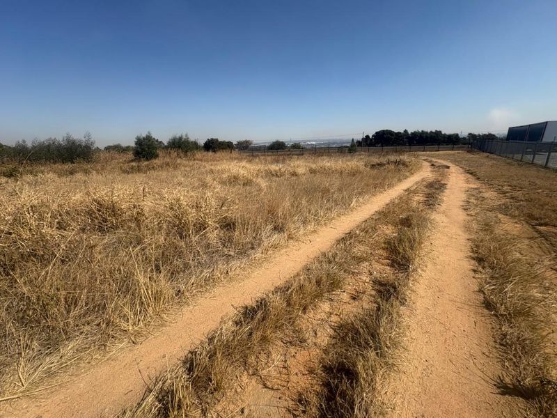An expansive undeveloped industrial land parcel featuring a dirt access track and perimeter fencing, offering significant potential for future development.