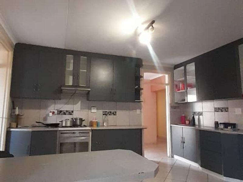 A functional kitchen featuring dark grey cabinetry, tiled flooring, a tiled backsplash, and integrated cooking appliances including an oven and extractor fan.