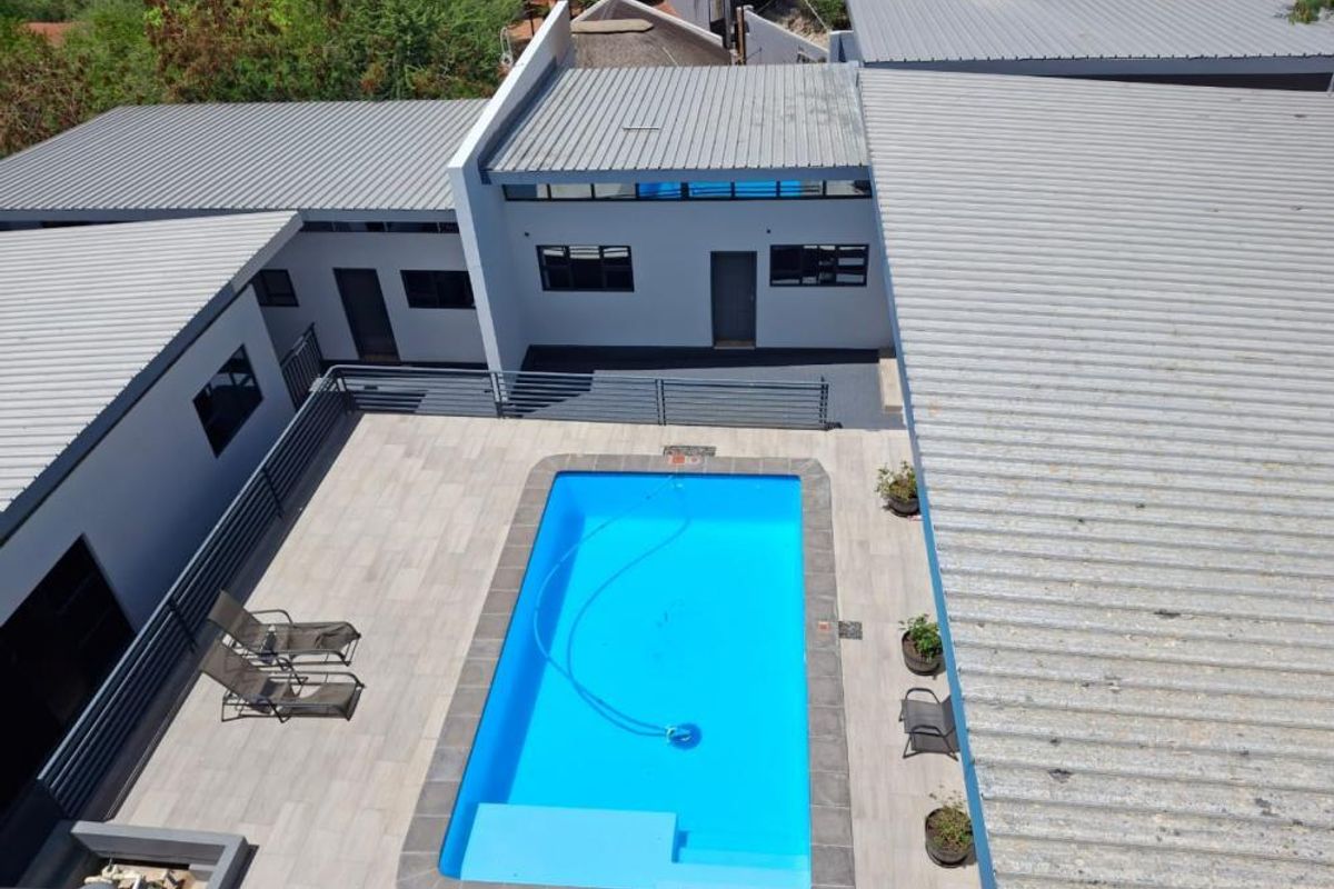 Aerial view of a modern property featuring a central swimming pool, tiled patio area, and corrugated metal roofing.