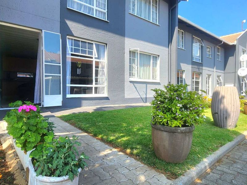 Front exterior view of a townhouse complex featuring a paved walkway, manicured lawn, and multi-pane windows with direct access to the unit.