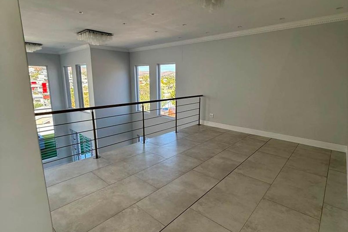 Spacious open-plan mezzanine living area featuring large windows, modern tiled flooring, and a sleek metal balustrade overlooking the lower level.