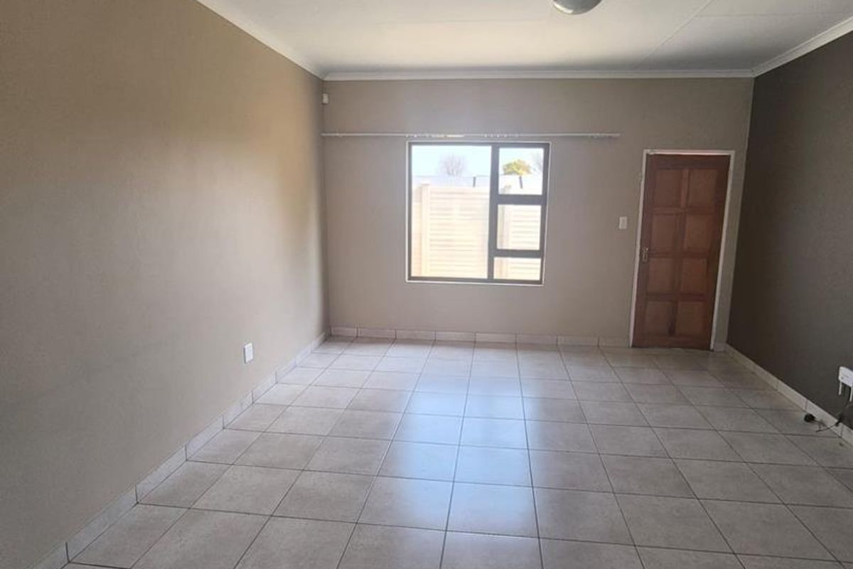 A spacious, empty living area featuring neutral tiled flooring, a large window, and a wooden door, providing a blank canvas for interior design.