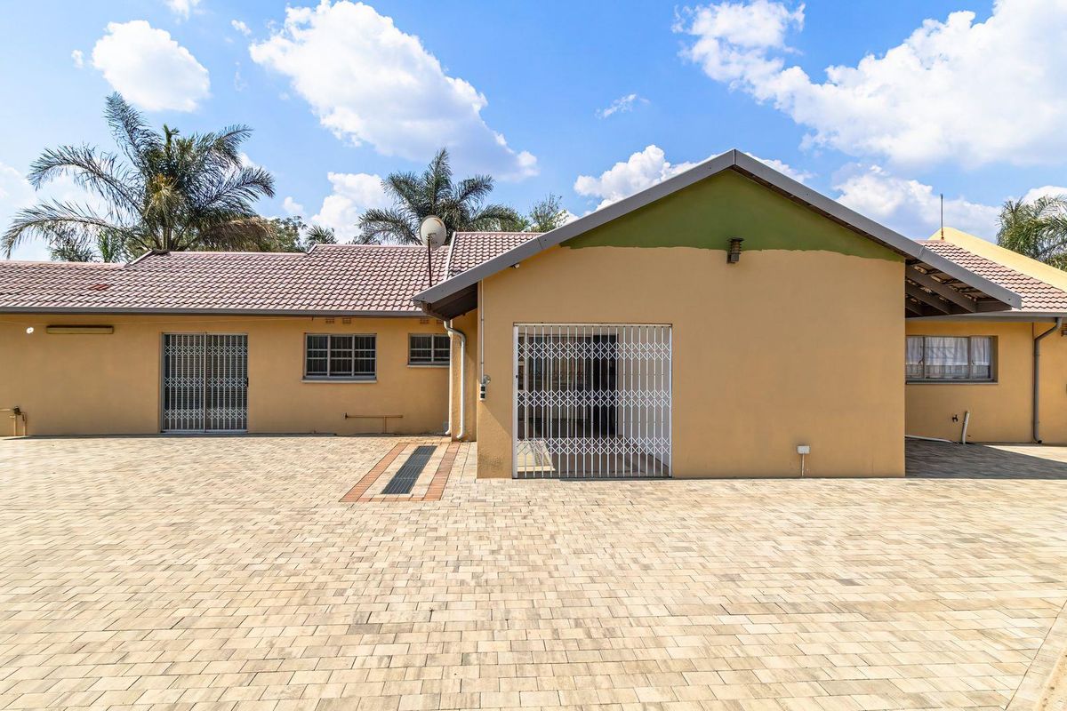 Rear exterior view of the house featuring a large paved courtyard, security gates on entrances, and a tiled roof structure.
