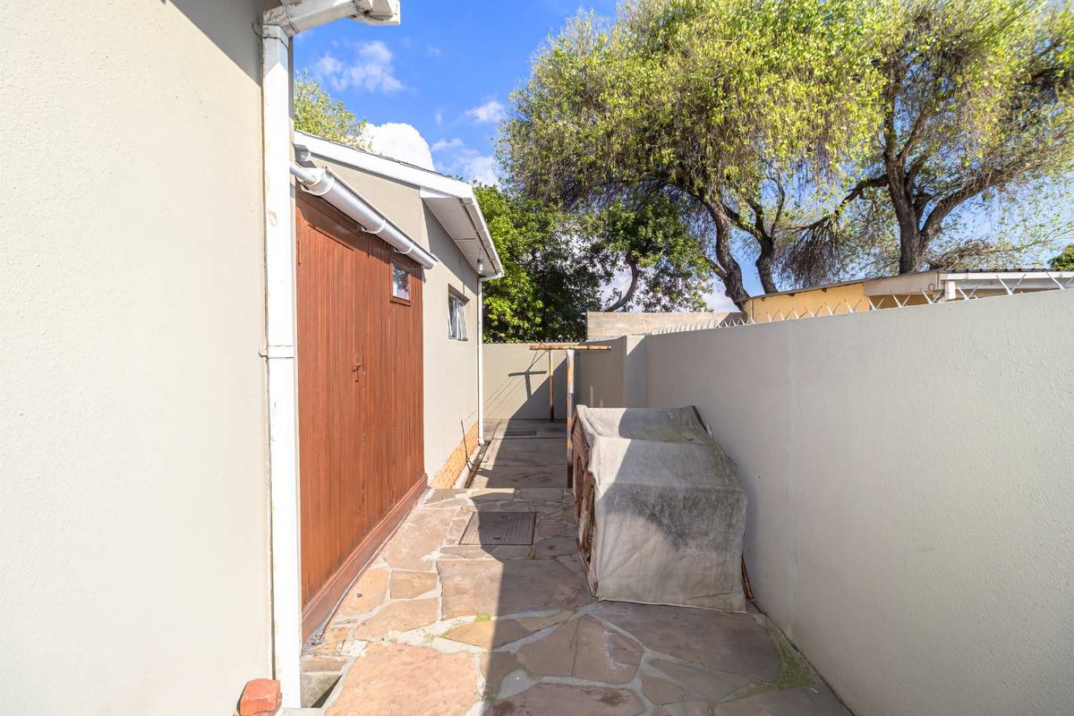 A side exterior walkway featuring stone paving, a perimeter wall with security spikes, and a functional rainwater gutter system.