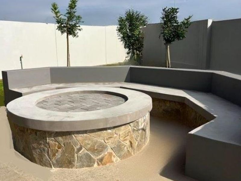 Outdoor entertainment area featuring a circular stone-clad fire pit with integrated concrete bench seating and paved flooring.