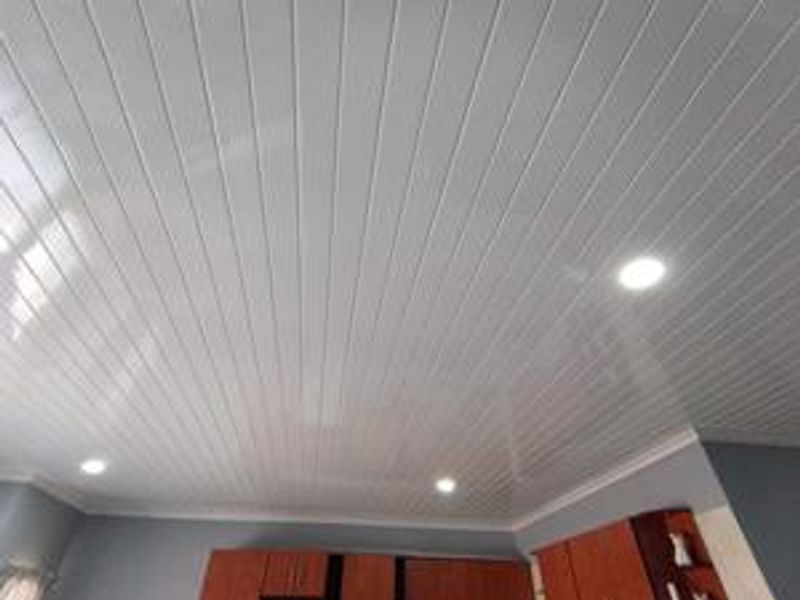 A kitchen interior featuring a modern white PVC panelled ceiling with integrated recessed downlights and decorative crown molding.