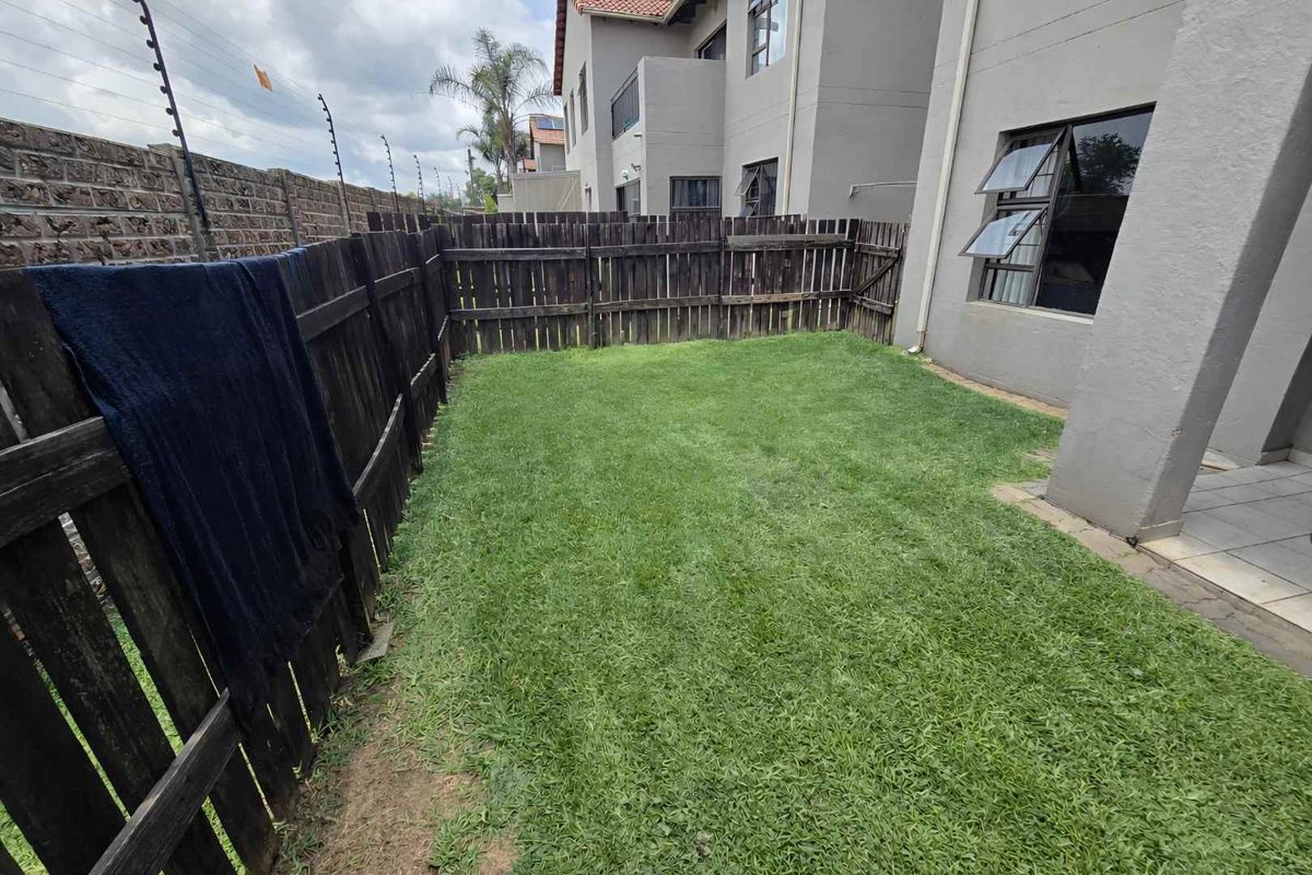 A private rear garden featuring a grass lawn, enclosed by timber fencing and adjacent to the townhouse exterior wall.
