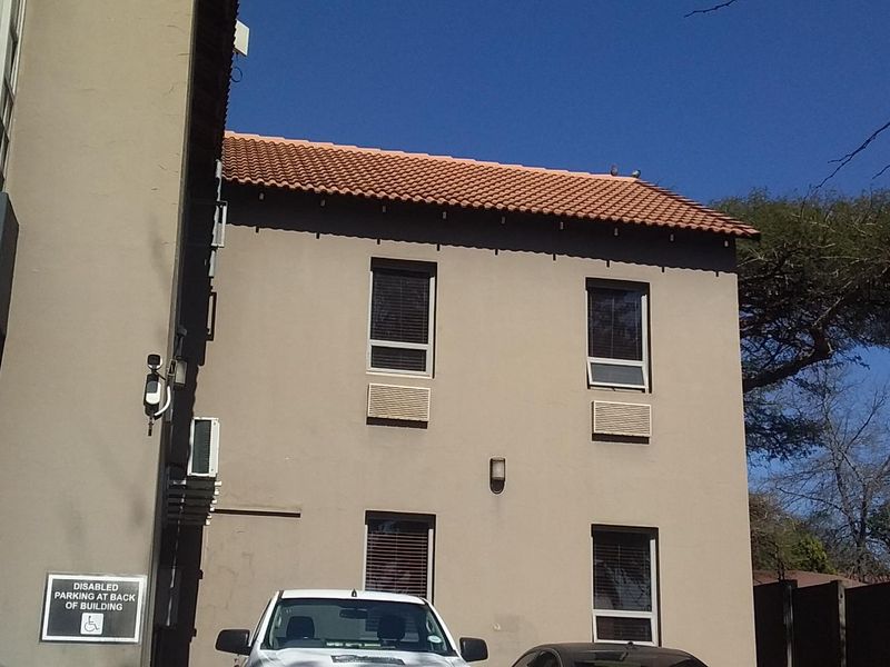 Exterior view of a commercial building facade featuring terracotta roof tiles, window-mounted air conditioning units, and paved parking area.