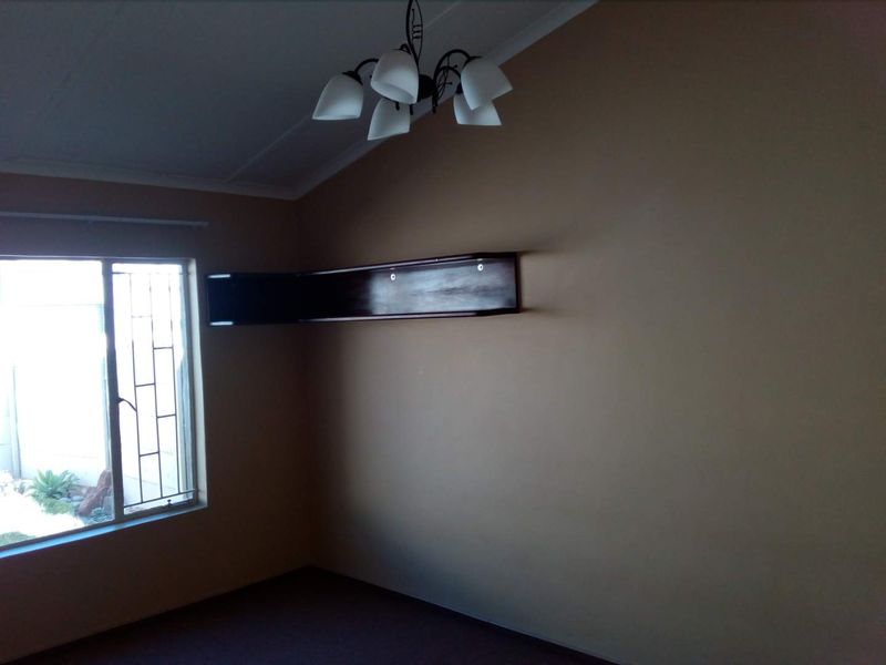 A vacant bedroom featuring neutral walls, a built-in corner shelf, and a window fitted with security bars.