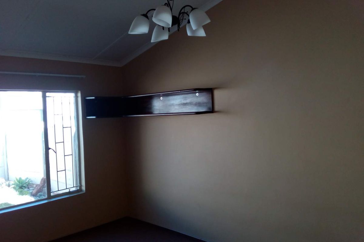 A vacant bedroom featuring neutral walls, a built-in corner shelf, and a window fitted with security bars.