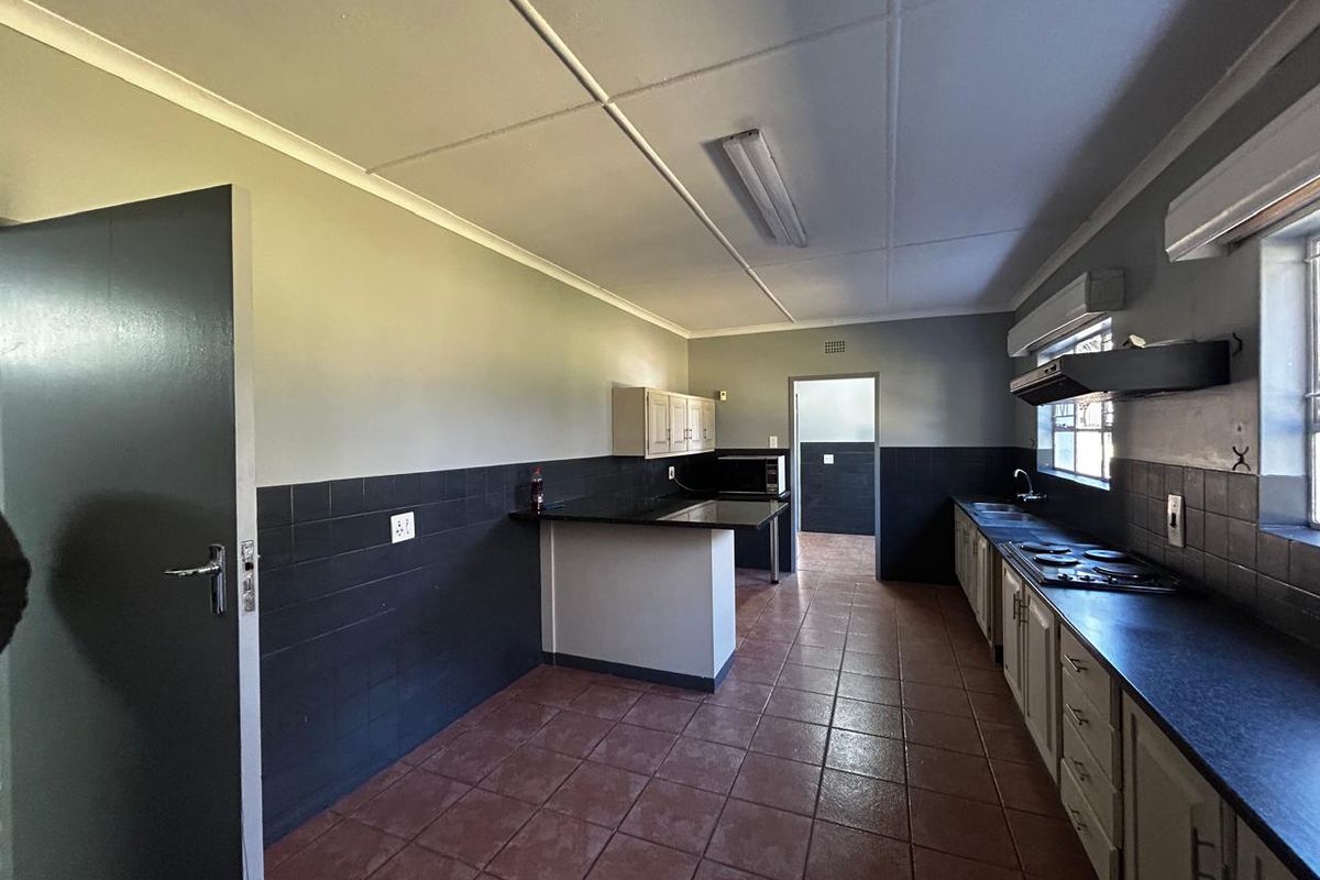Spacious kitchen featuring built-in cabinetry, dark tiled splashbacks, a hob with extractor fan, and durable tiled flooring throughout.