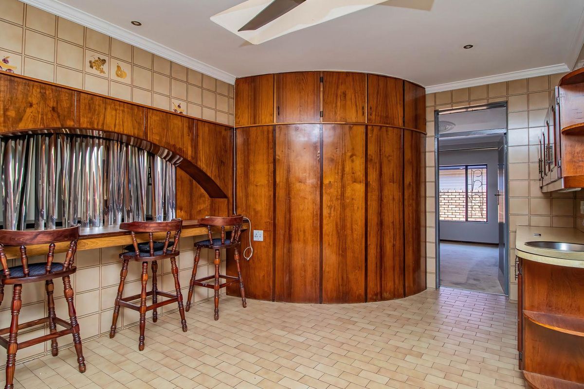 A dated kitchen featuring extensive built-in wooden cabinetry, a breakfast bar, tiled splashbacks, and a stainless steel sink.