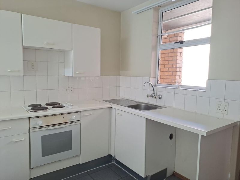 A functional kitchen featuring white cabinetry, a built-in oven and hob, tiled backsplash, and a stainless steel sink with a window view.