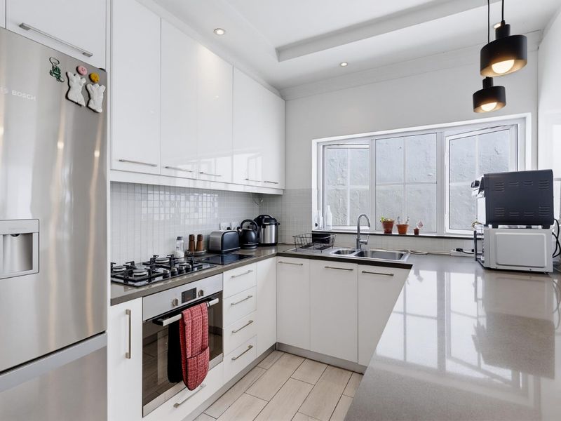 Modern kitchen featuring high-gloss white cabinetry, stone countertops, gas hob, built-in oven, and tiled flooring with ample natural light.