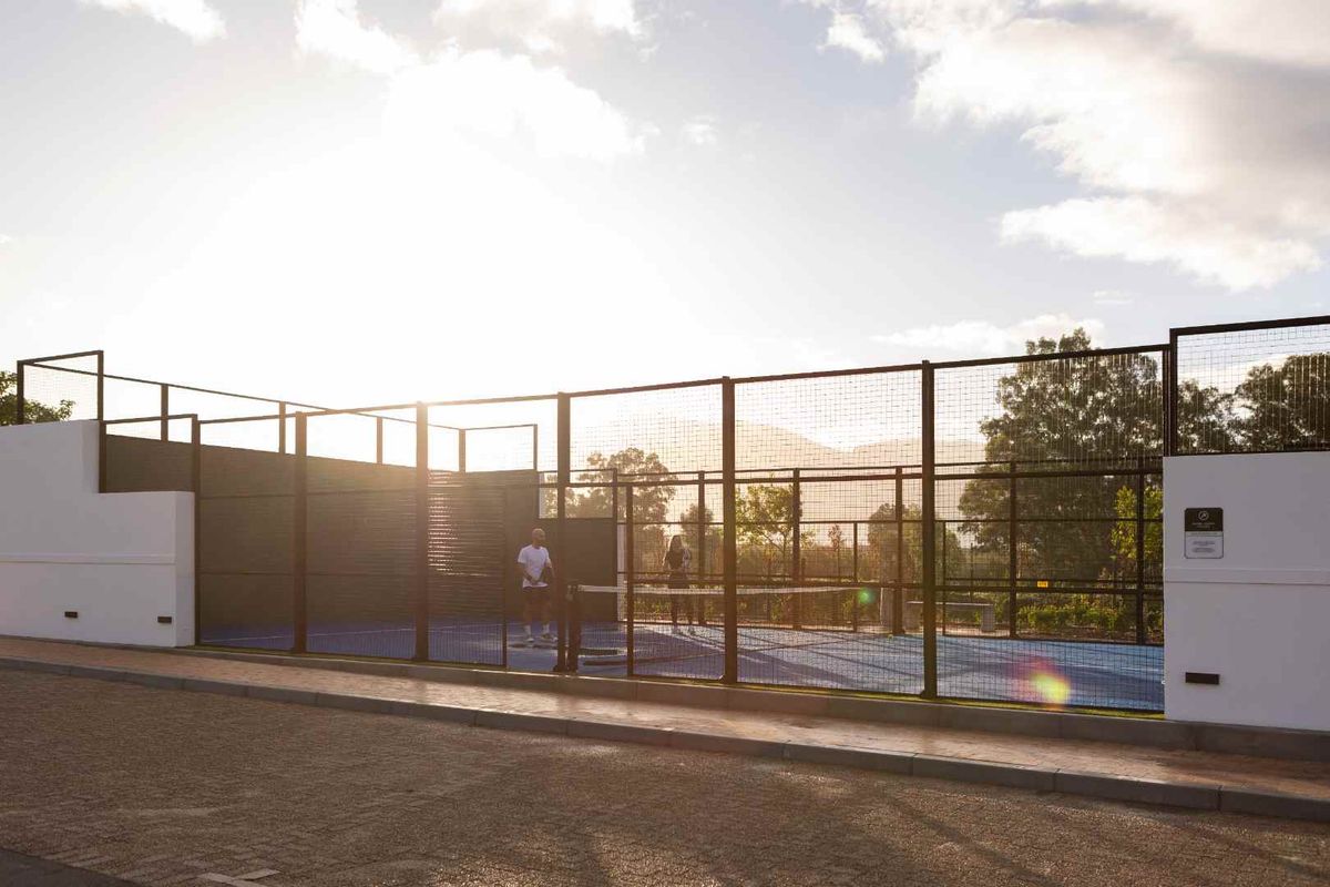 A well-maintained outdoor padel court featuring a blue synthetic surface, perimeter fencing, and integrated lighting, suitable for recreational sports.
