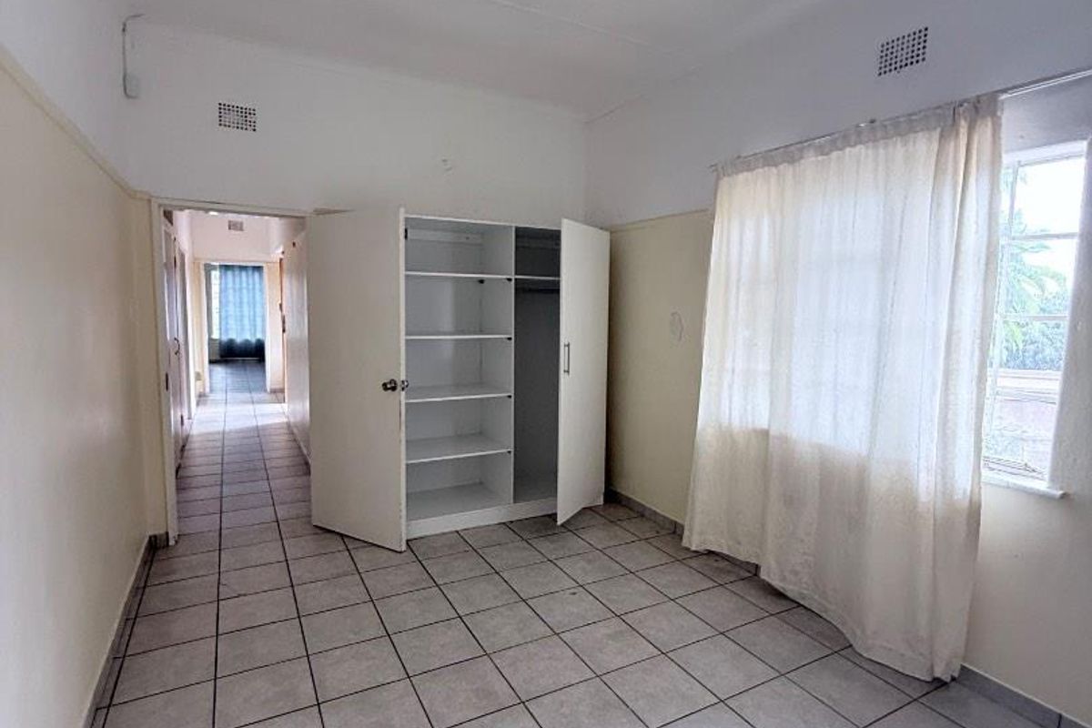 A bedroom featuring tiled flooring, a built-in wardrobe, and access to a hallway, offering a functional space with potential for cosmetic updates.