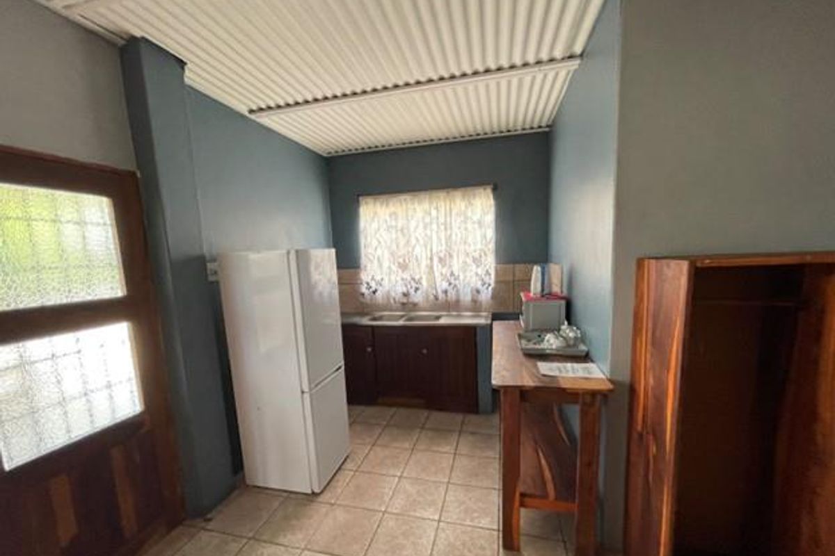 A functional kitchenette area featuring tiled flooring, built-in cabinetry with a sink, and direct access to the exterior via a wooden door.