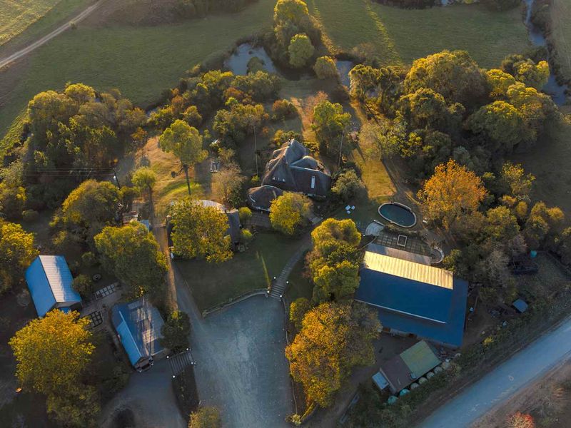 Aerial view of the guest house property featuring multiple buildings, a swimming pool, mature trees, and extensive landscaped grounds in a rural setting.