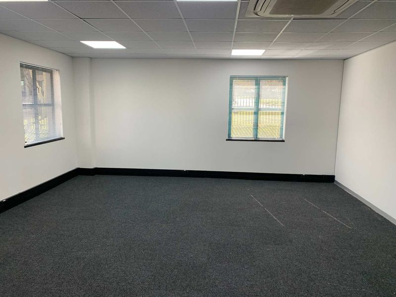 A clean, empty office space featuring grey carpeting, suspended ceiling with recessed lighting, integrated air conditioning, and windows with fitted venetian blinds.
