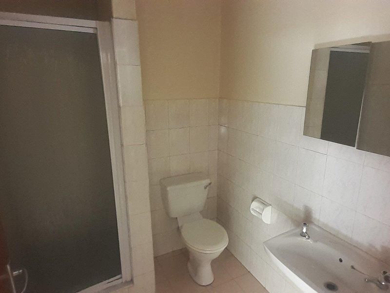 A functional bathroom featuring a shower enclosure, pedestal basin, and wall-mounted mirror cabinet, finished with tiled walls.
