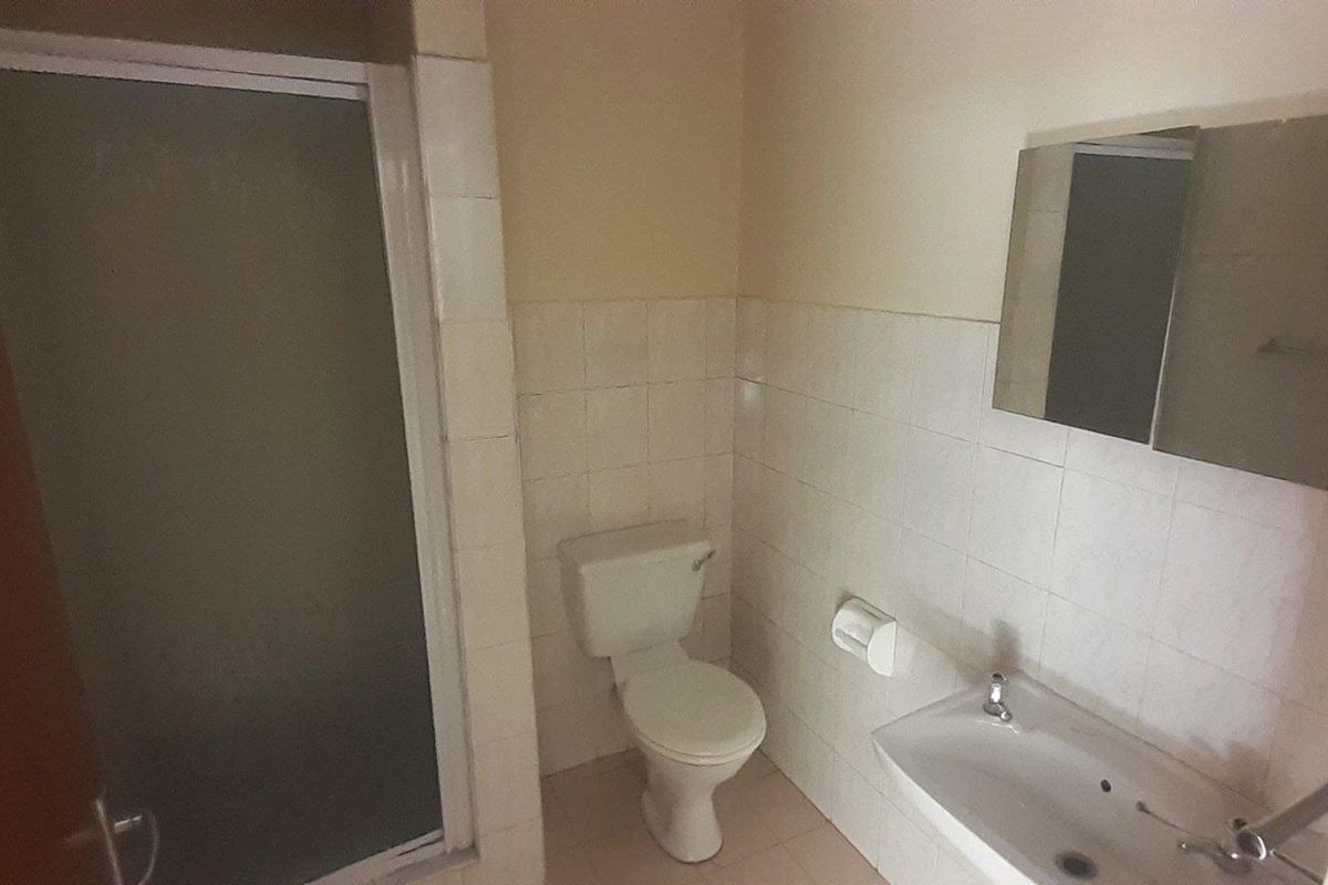 A functional bathroom featuring a shower enclosure, pedestal basin, and wall-mounted mirror cabinet, finished with tiled walls.