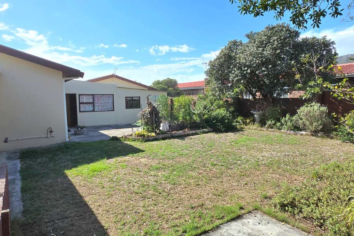 A spacious rear garden featuring a lawn area, established perimeter landscaping, and a paved section adjacent to the main dwelling.