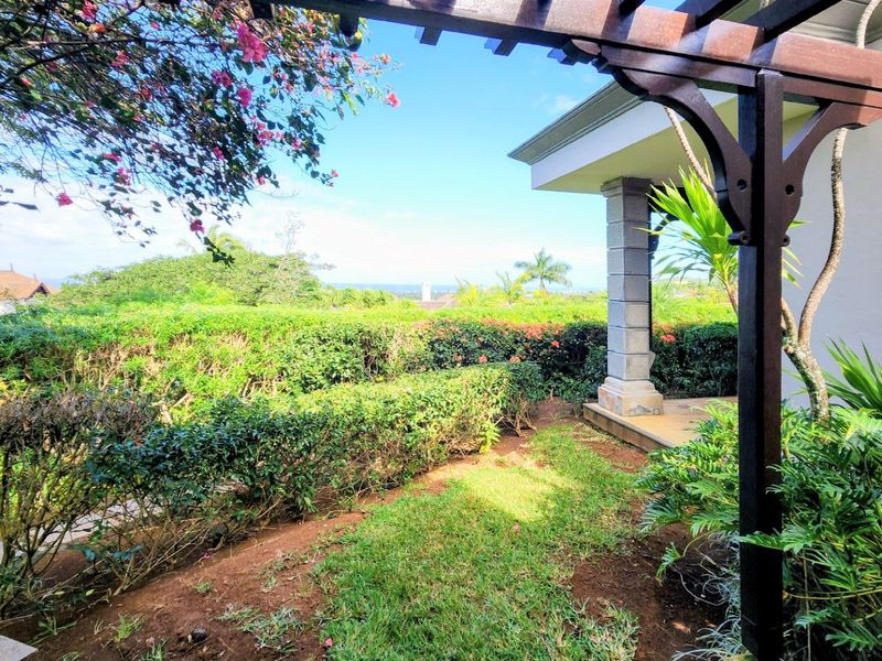 A covered patio area featuring a timber pergola and stone pillar, overlooking a well-maintained garden with distant views.