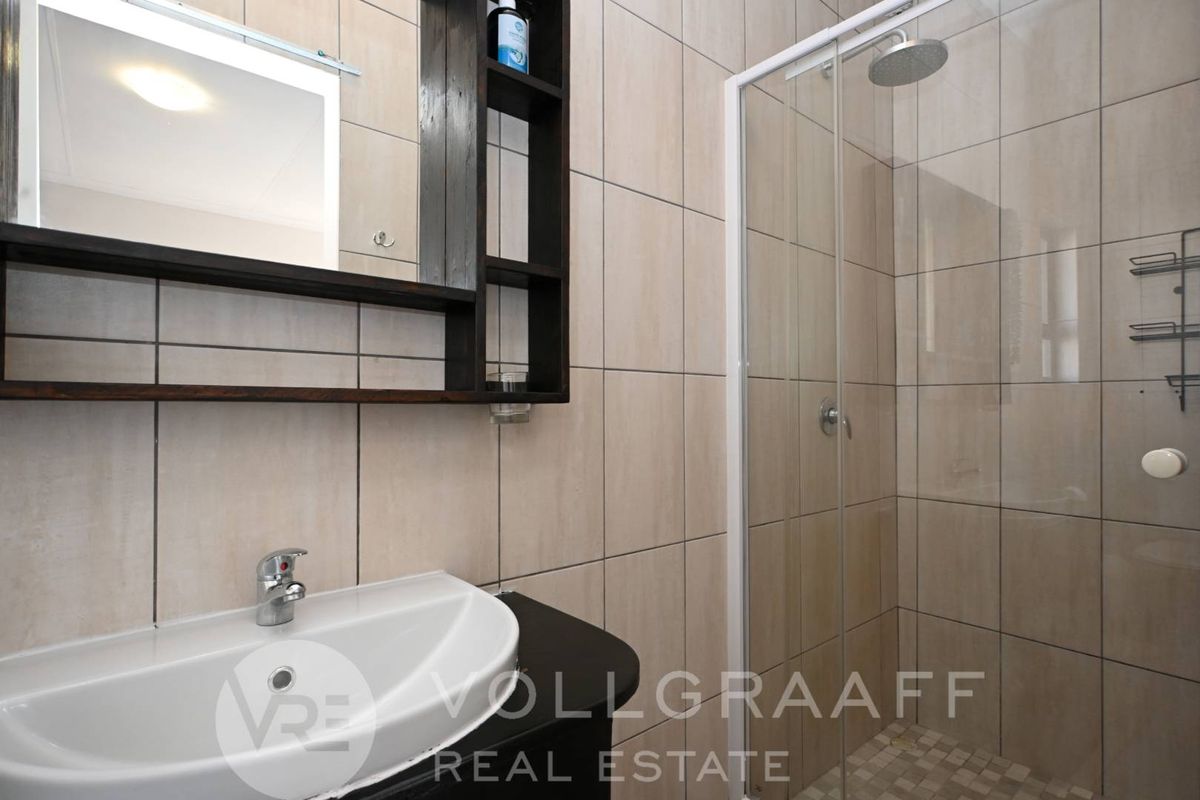 A modern bathroom featuring a glass-enclosed shower, a wall-mounted vanity with a basin, and neutral floor-to-ceiling wall tiles.