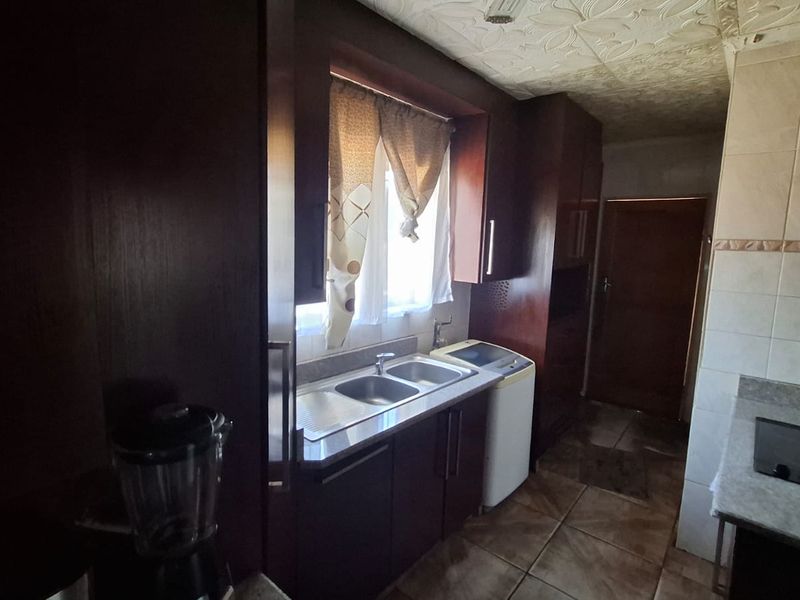 A functional kitchen featuring dark wood cabinetry, a double sink, integrated hob, and extractor fan, with tiled flooring and splashbacks throughout.