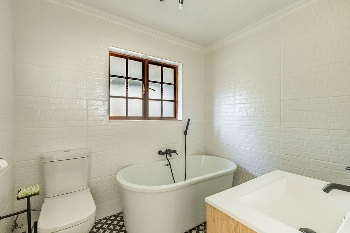 Modern bathroom featuring a freestanding bathtub, handheld shower mixer, vanity with basin, and stylish patterned floor tiles with white brick-style wall tiling.